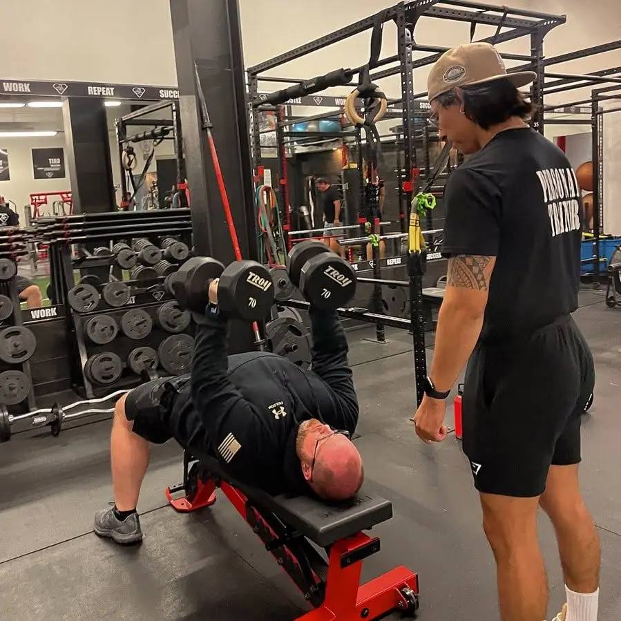 A coach watching a client press dumbbells